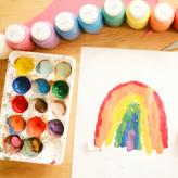 A palette with paints in it and a paper with a rainbow painted.