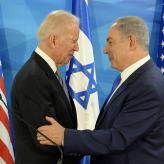 Two men in suits standing in front of the Israeli and US flags