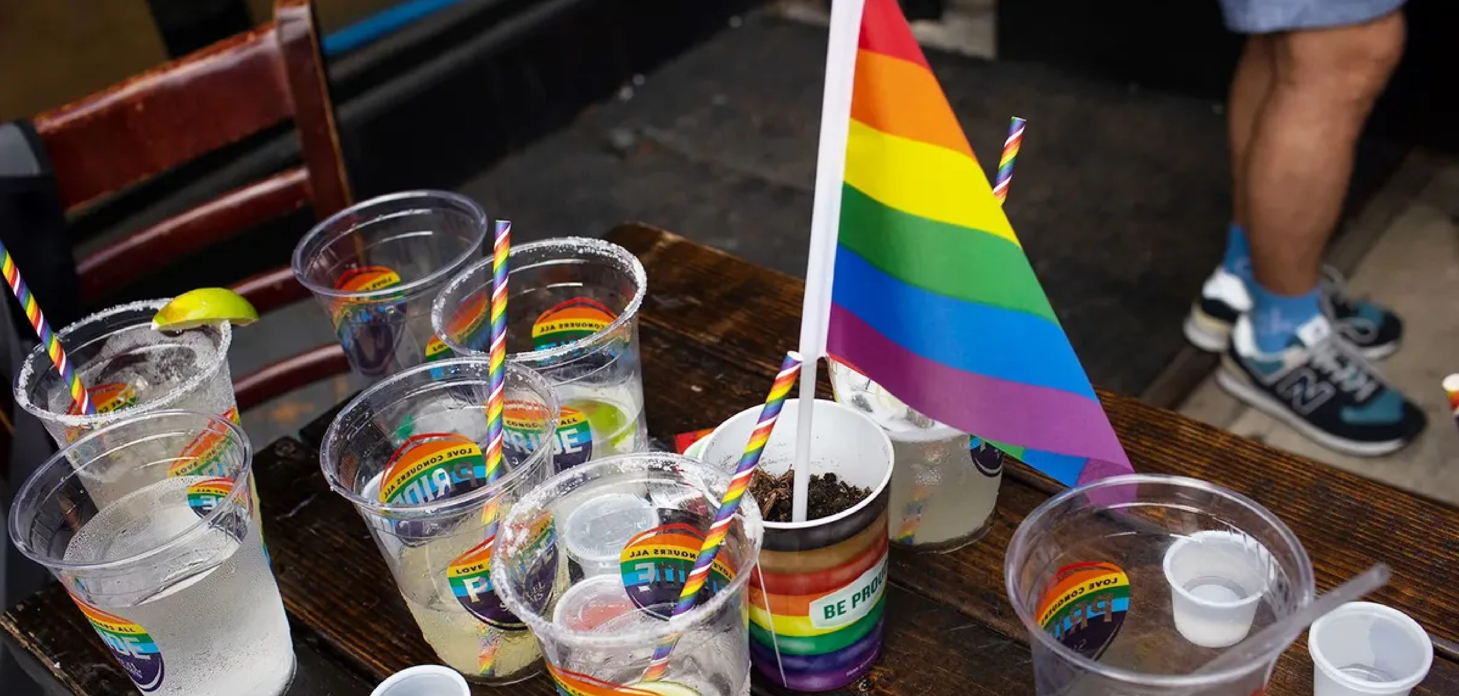 A table with plastic cups that have stickers on them that say "Pride." One of the cups has a rainbow flag in it.