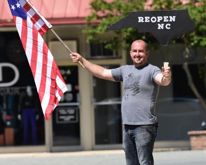 A white man holding an american flag in one hand and a board that says reOpen NC in another.