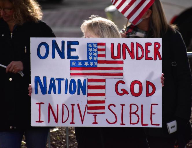 A person holding an image that says "One nation under god" around a cross that bears the colors of the American flag