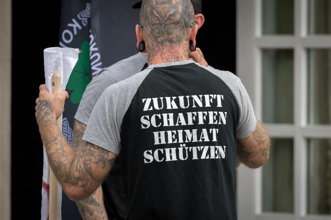 The back of a man wearing a black t shirt that reads "Zukunft Schaffen Heimat Schützen." Which translates to "Creating the future, protecting the home."