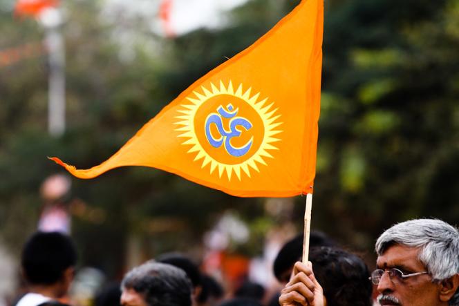 A man holding a saffron triangular flag with an "om" symbol on it.