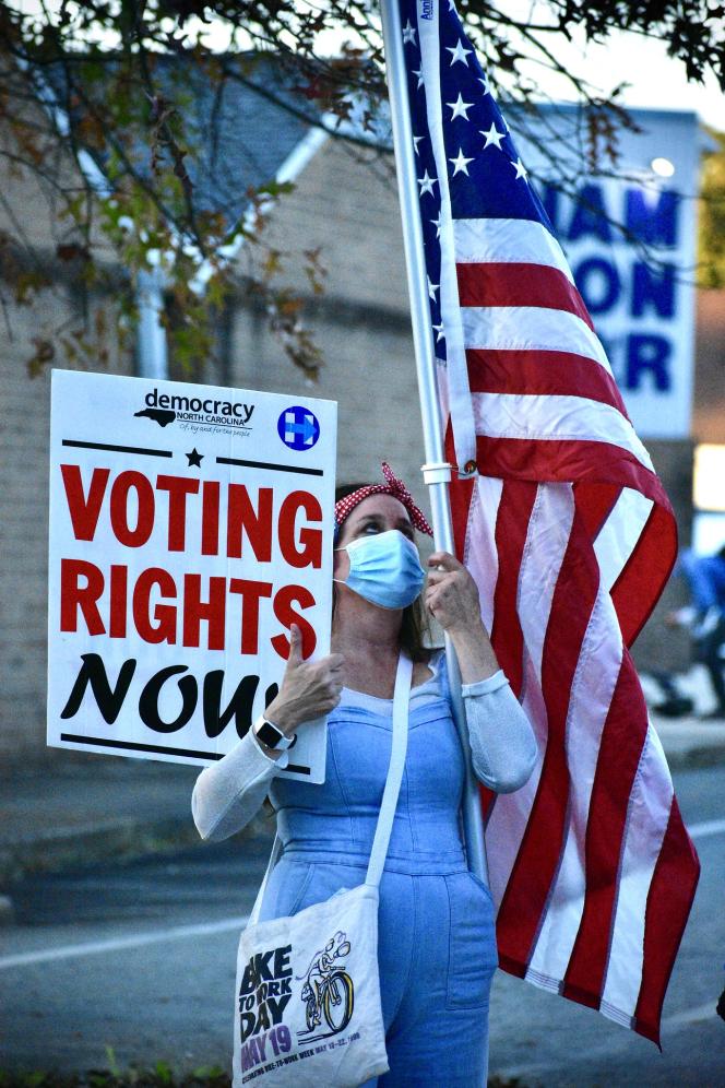 A woman holding a sign that says "Voting rights now" and an american flag