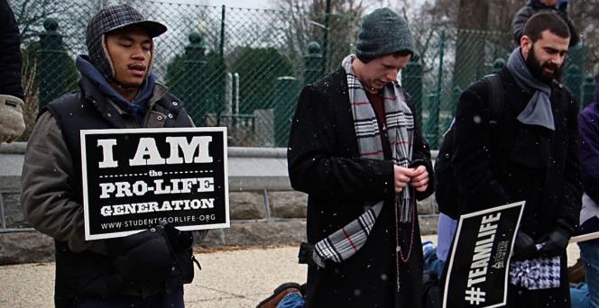 Three men standing in jackets holding signs that say "I am the pro-life generation" and "#TeamLife"