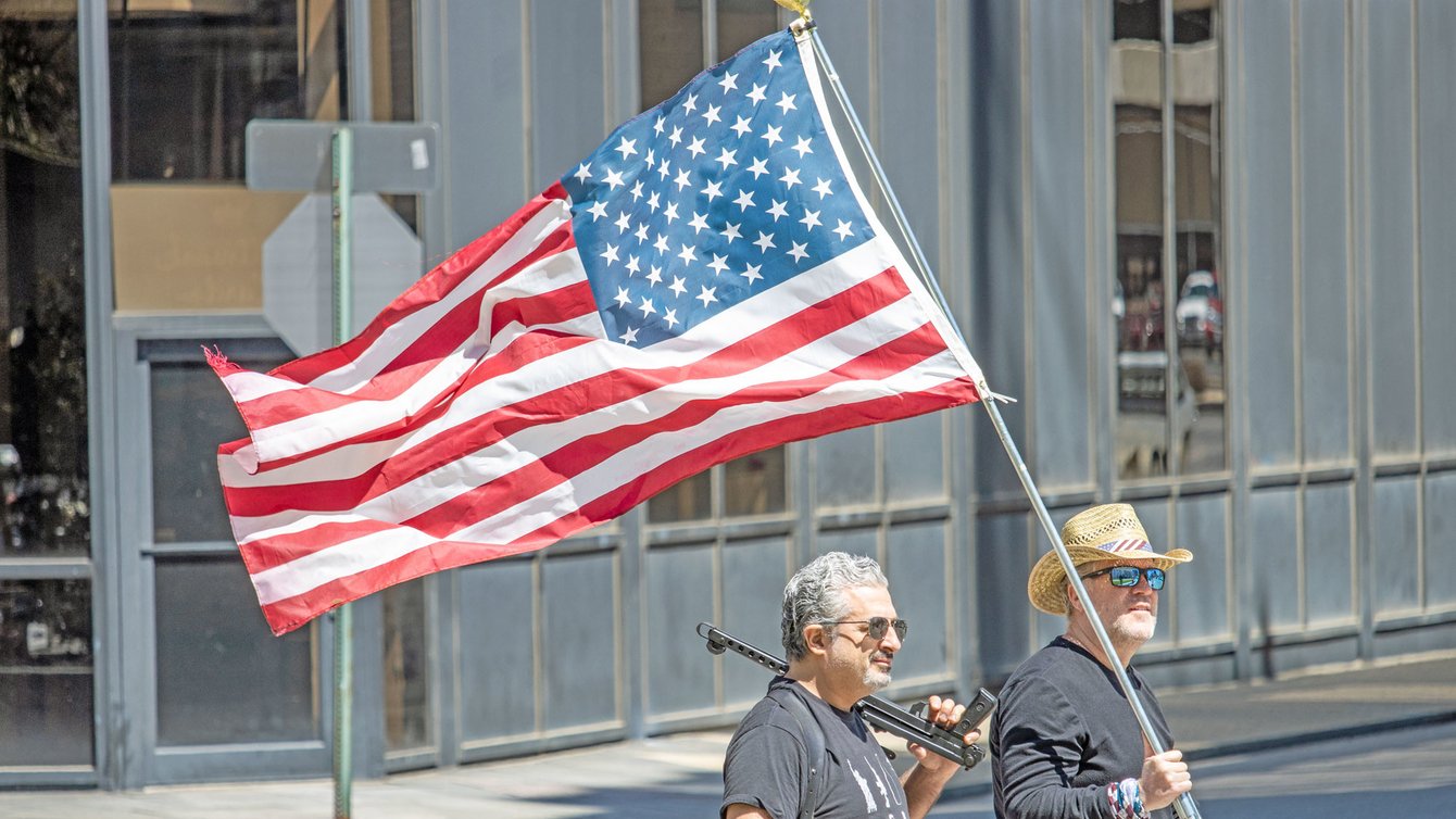 Coronavirus lockdown protestors hold American flag and gun, April 21, 2020 (Credit: Becker1999/flickr)
