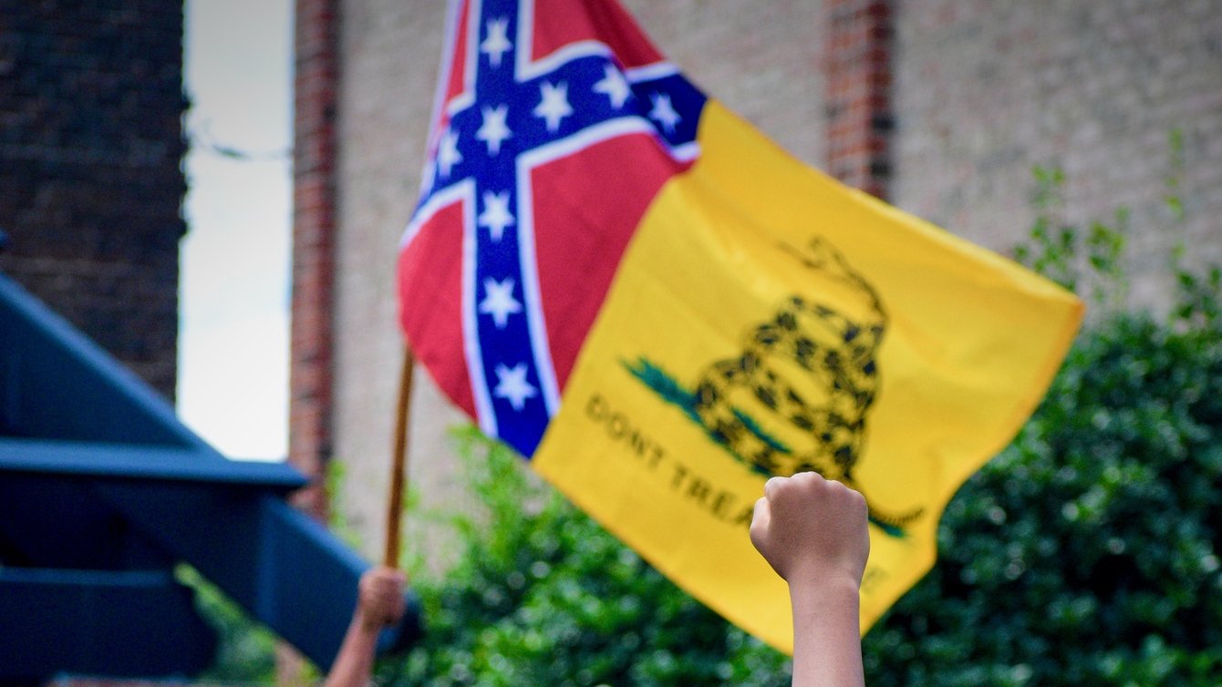 Pro-confederacy protestor holds up a confederate flag, a counter-protestor raises a fist in response. 
