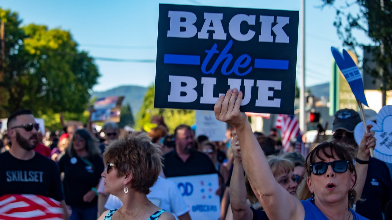 Protesters gathered. A woman holds up a sign that read Back the Blue.