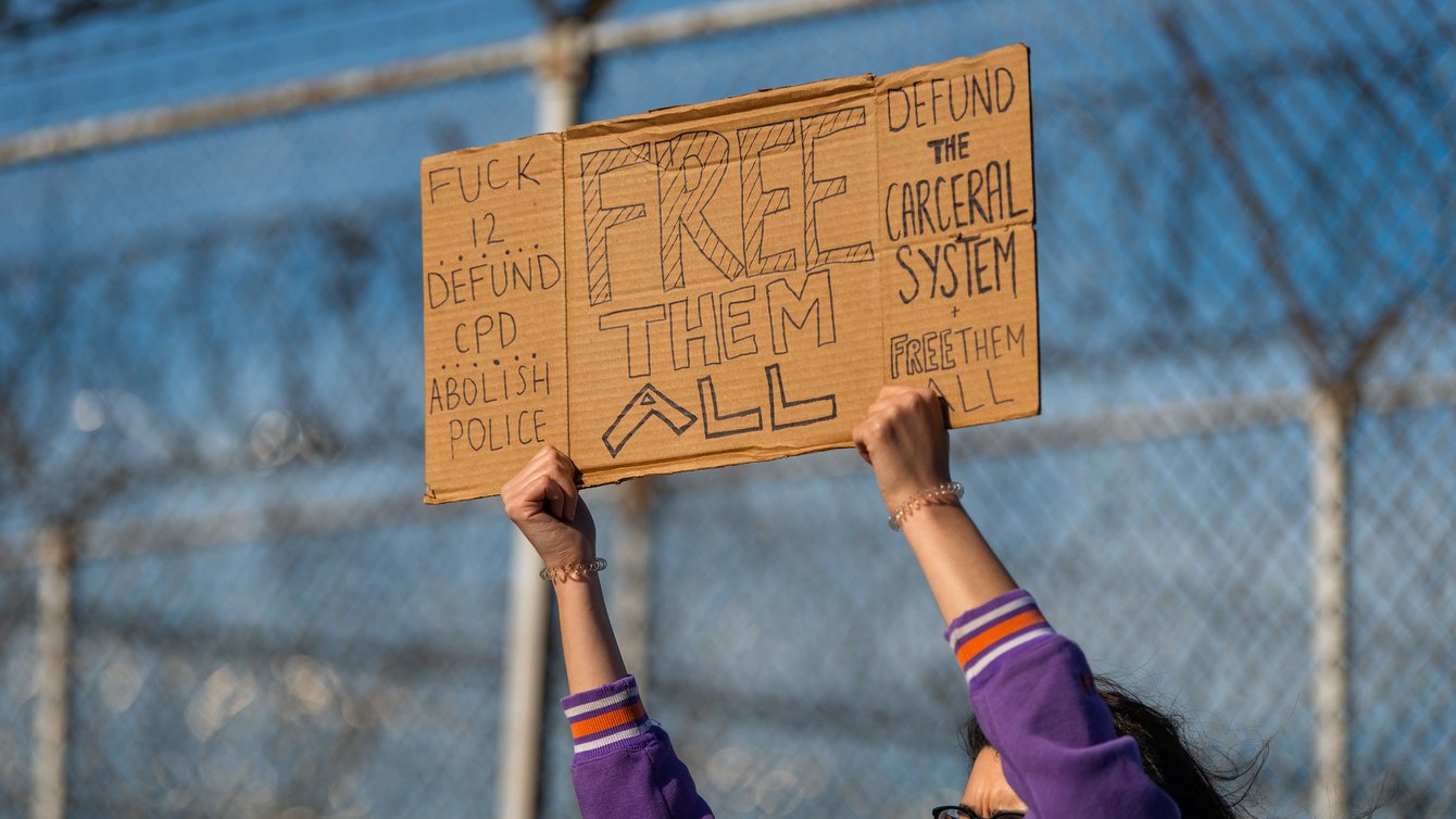 A sign on cardboard says "Fuck 12, Defund CPD, Abolish ICE, Free them All, Defund the Carceral System, Free them all"