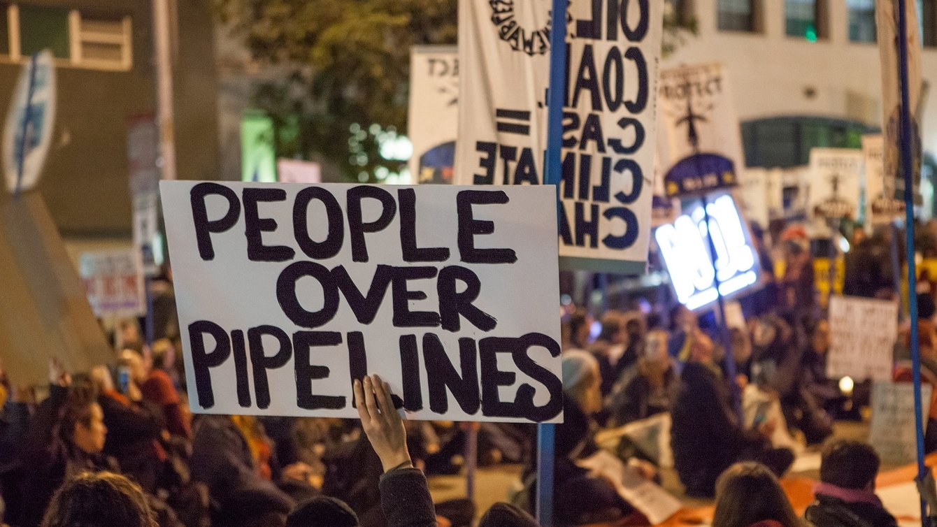 A protester holding a sign that reads "people over pipelines"