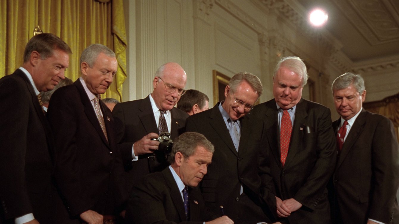 Presdient George Bush signing something, with men standing around him.