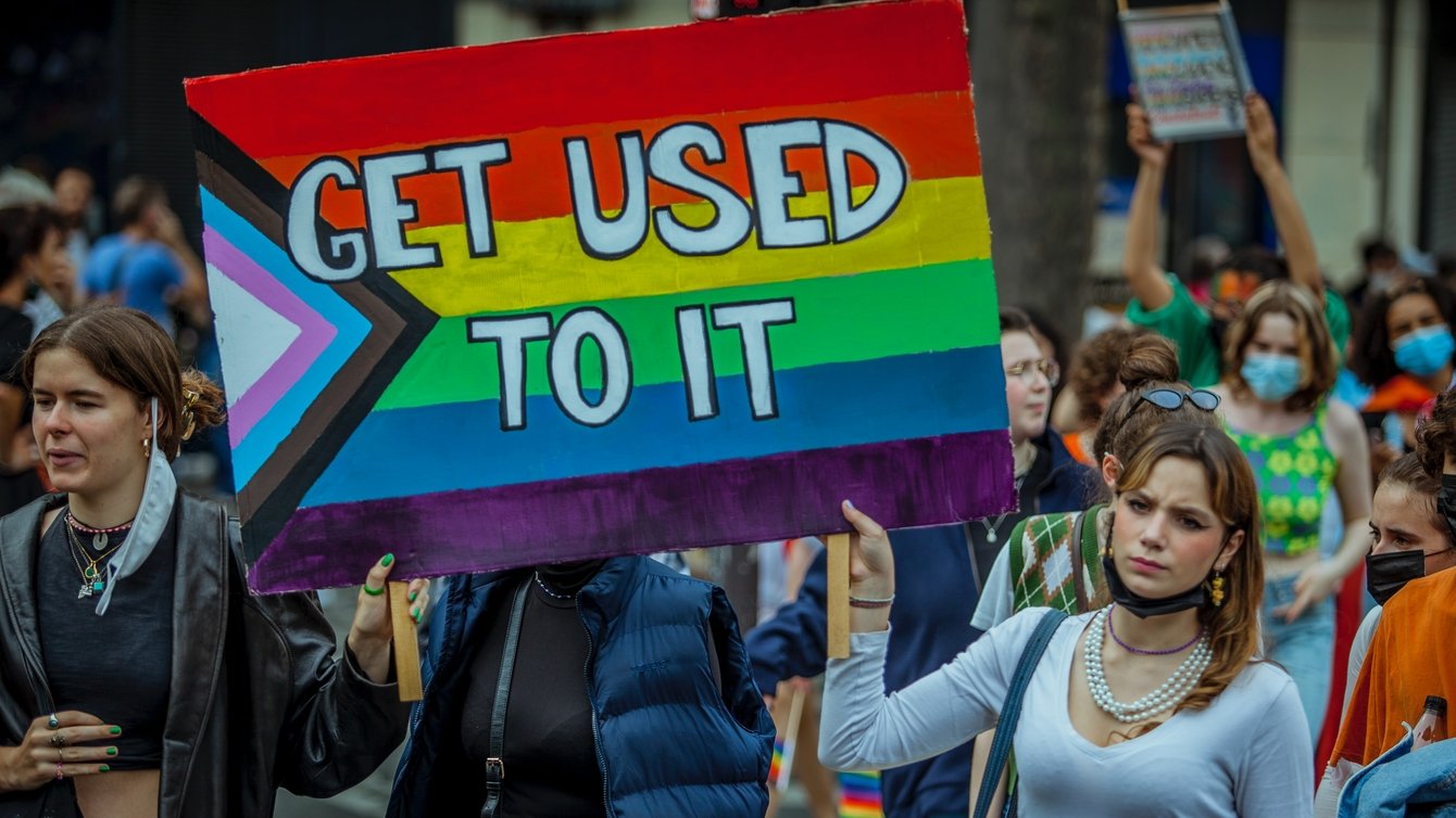 A woman at a Pride march in Paris holding a sign painting in the LGBT colors that says "Get used to it"
