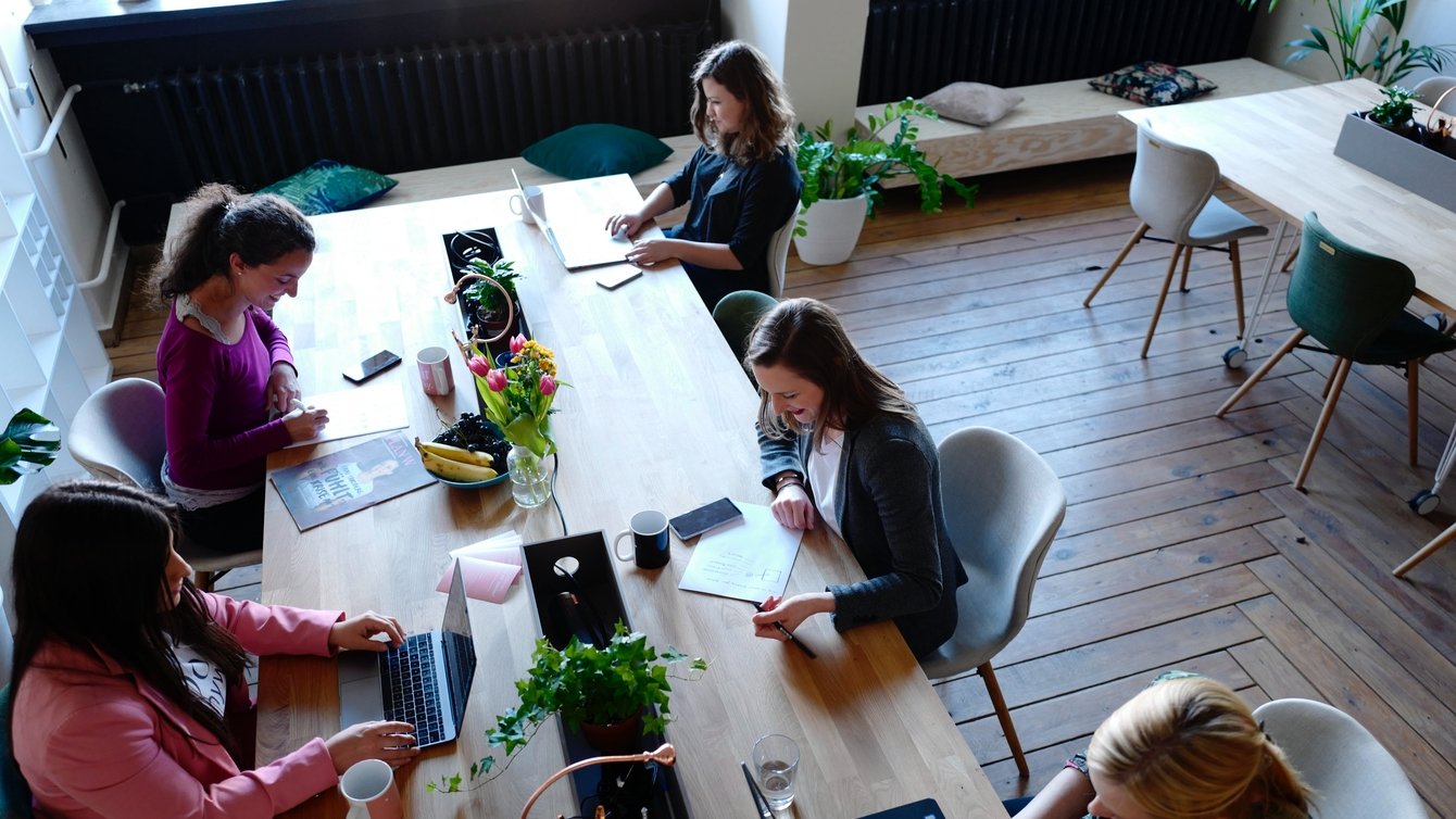 A group of women at a table, with computers and books.
