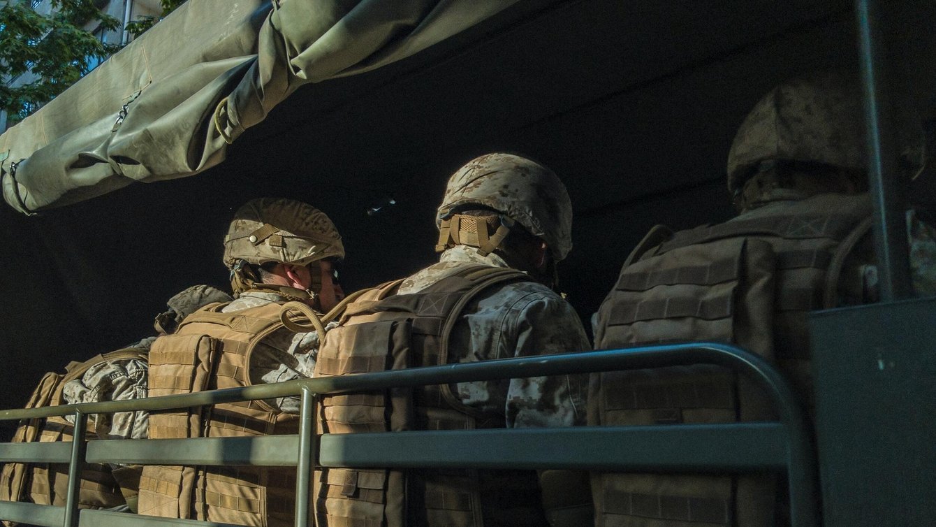 Men in a military uniform, sitting with their backs to us.