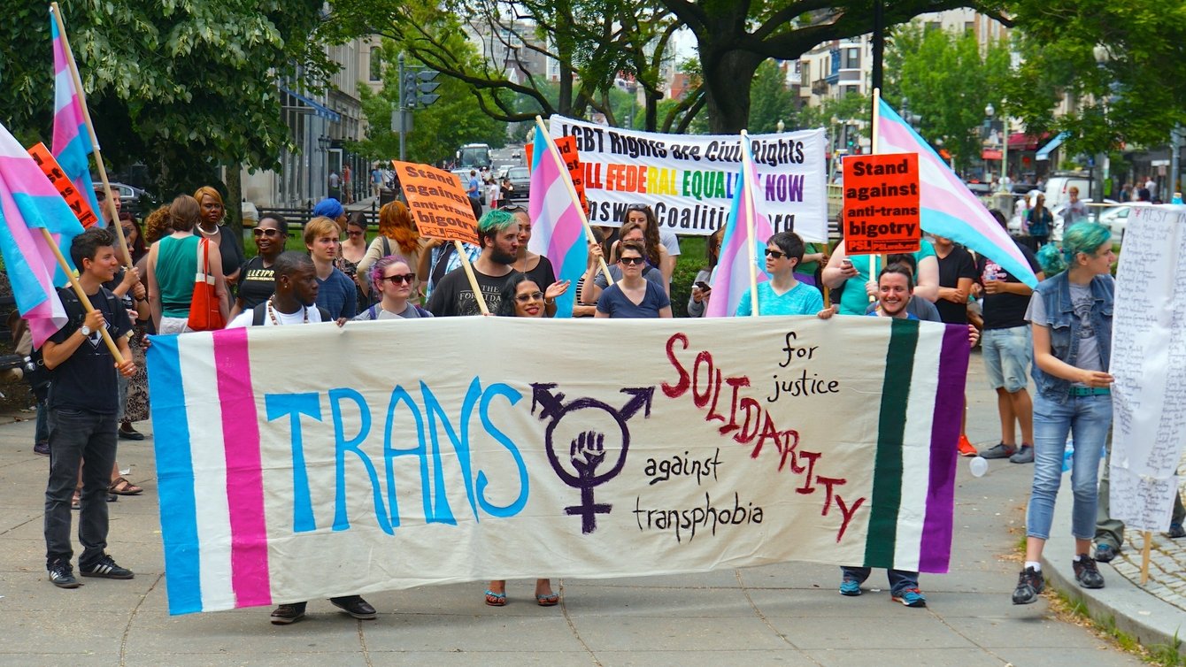 Protesters holding a banner that says Trans Solidarity against transphobia.