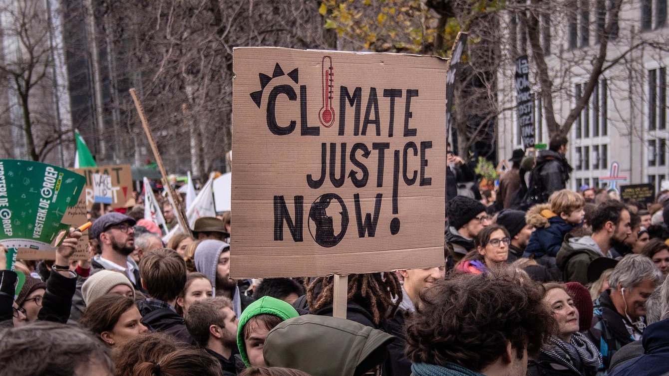 Protesters, and one protesters holding a board that reads "climate justice now!"