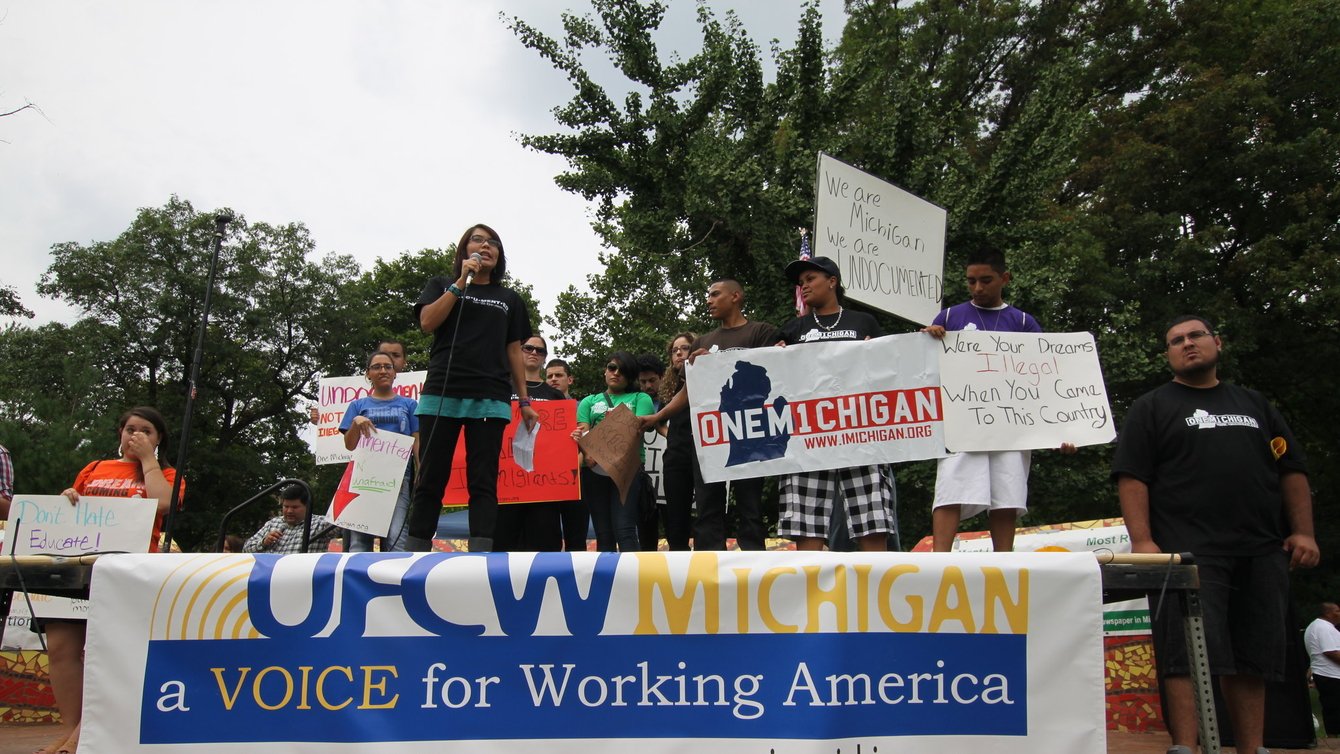People standing on a platform with a table in front of them with a banner hanging off the table that says "A voice for Working America."