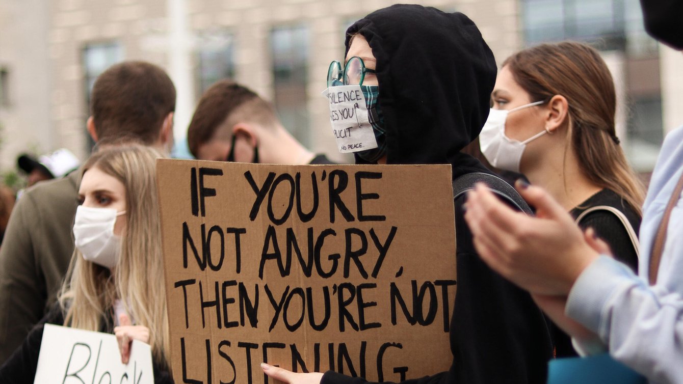 A person holding a sign that says "If you're not angry, then you're not listening."