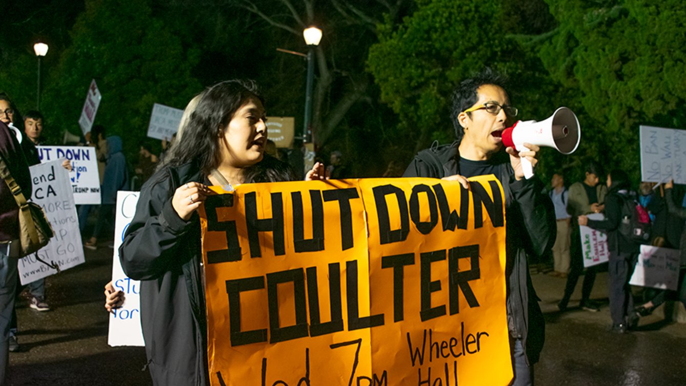 Two students holding a banner that says "Shut down Coulter. Wed 7 PM Wheeler Hall."