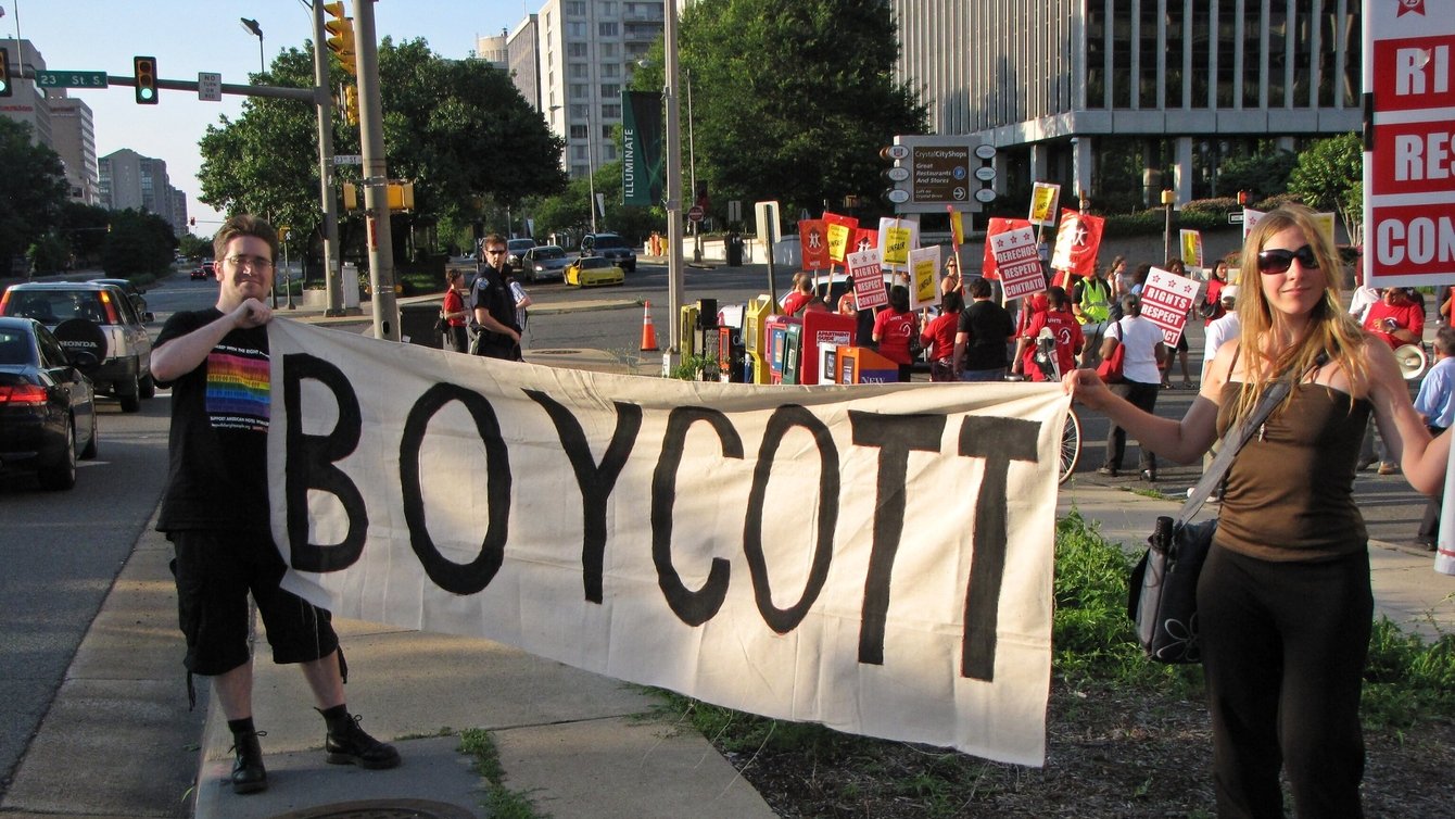 Two people holding a sign that says "Boycott" at a protest