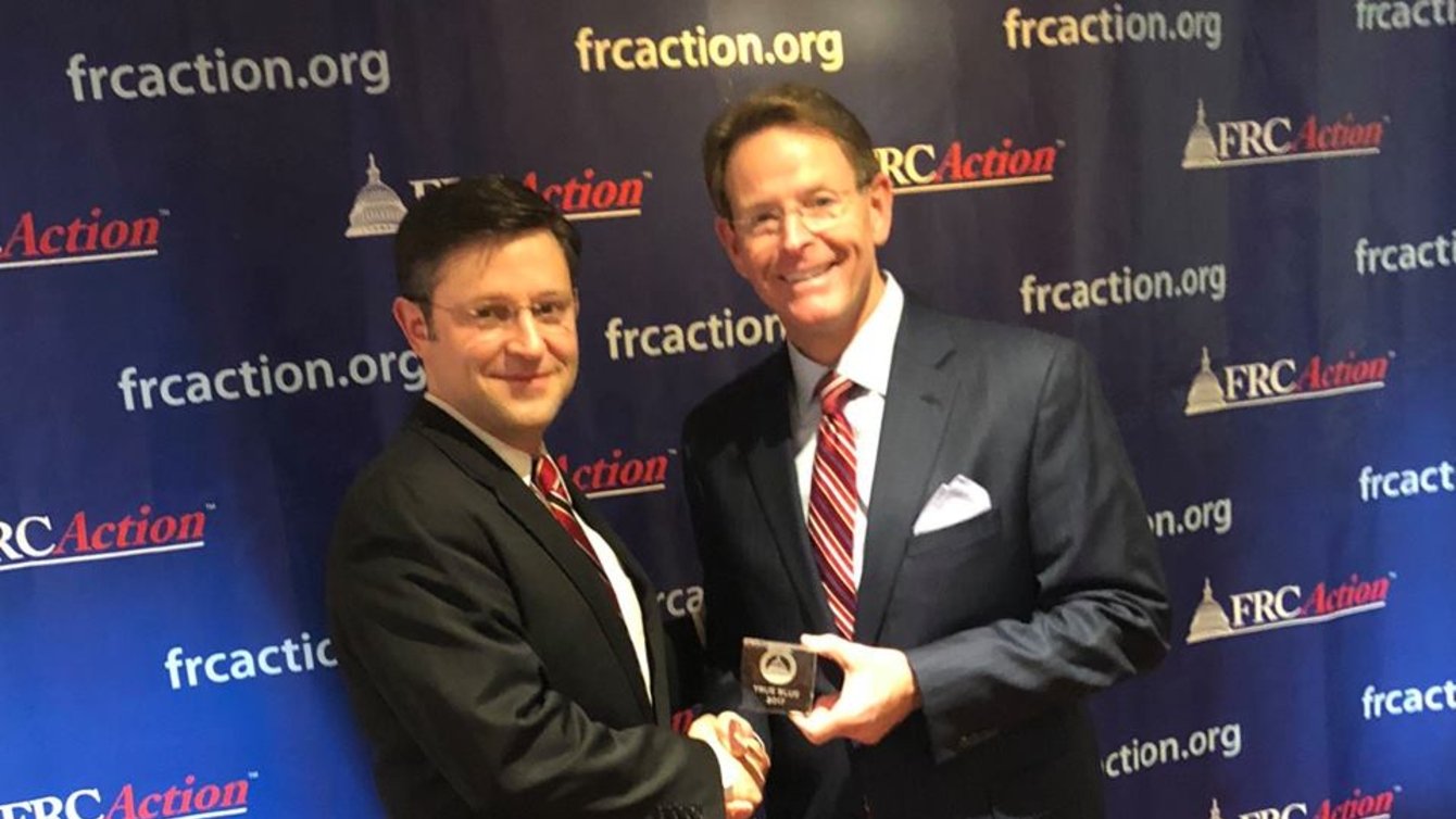 Two men in suits and glasses standing in front of a background saying "FRCAction"