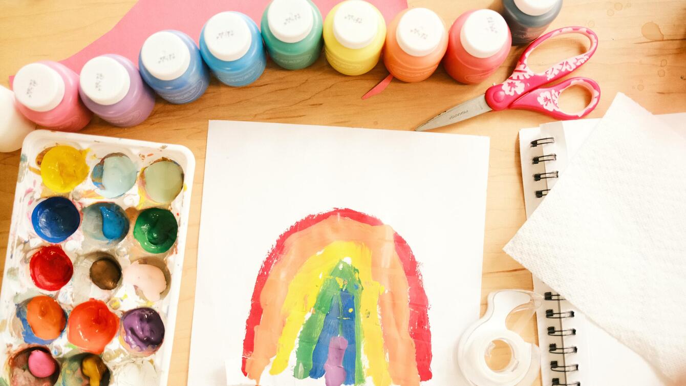 A palette with paints in it and a paper with a rainbow painted.