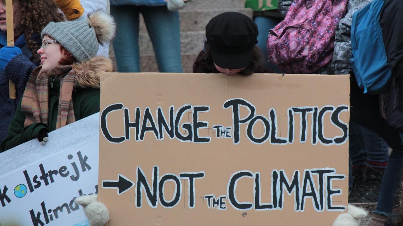 a protester with a sign that says "change the politics not the climate"