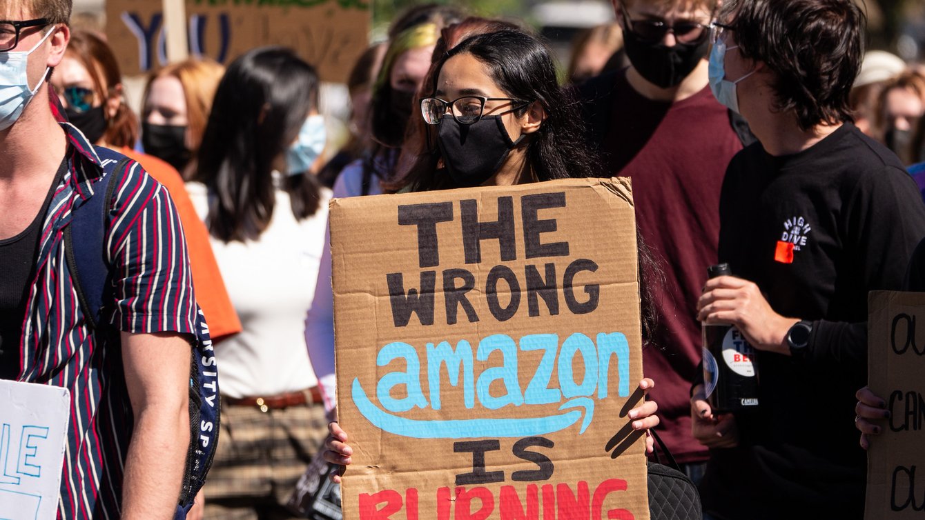 A person wearing a mask holding a sign saying "The wrong Amazon is burning"
