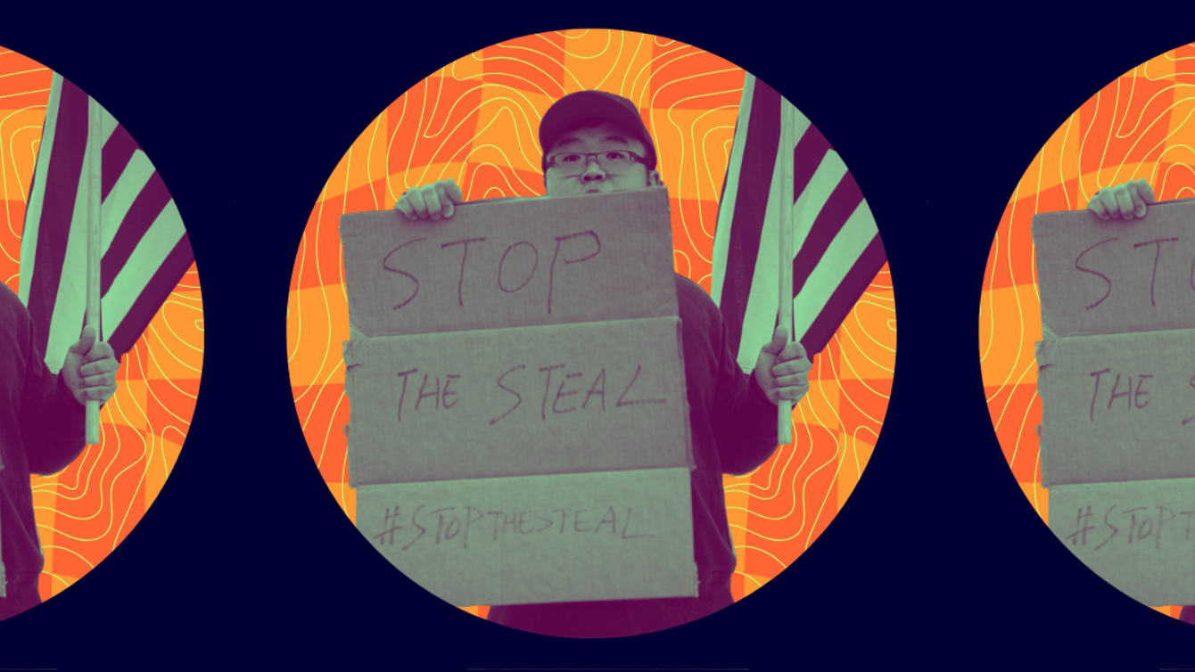 A protestor holds an American flag and a sign reading "Stop the Steal"
