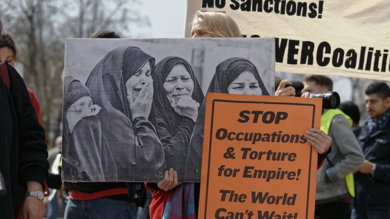 A person holding an image of women crying and a sign that says "stop occupations and torture for empire! The world can't wait!"