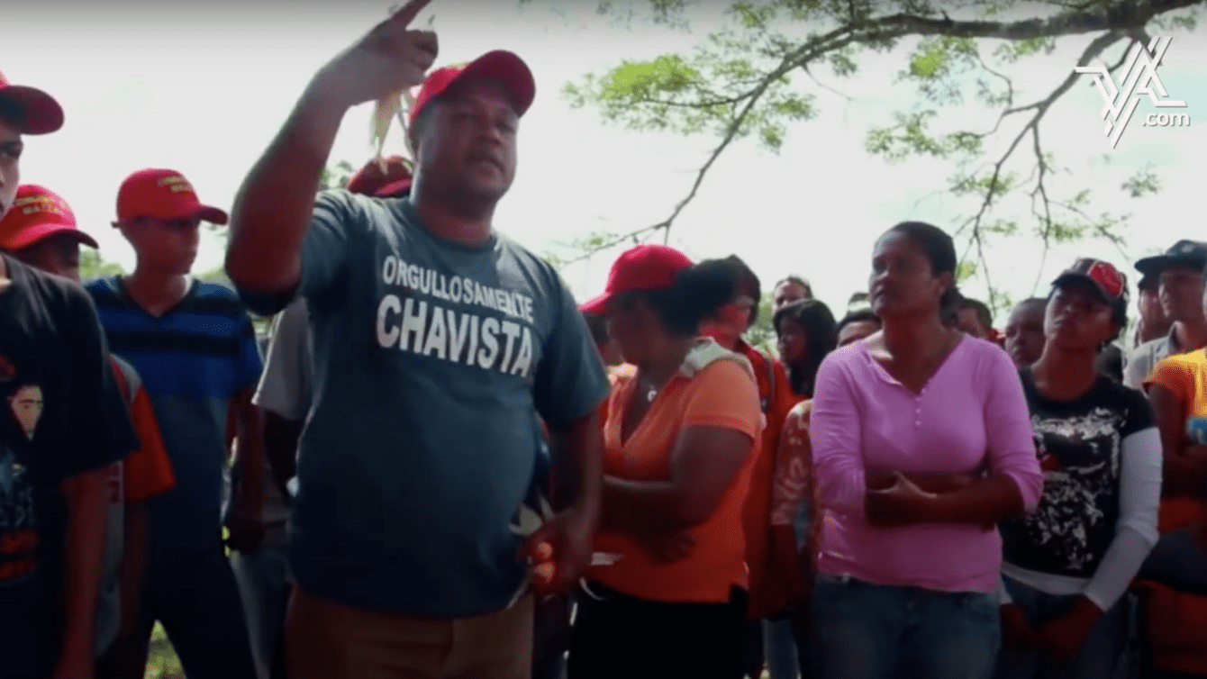 A group of people wearing red hats led by a man speaking with his hand raised. 