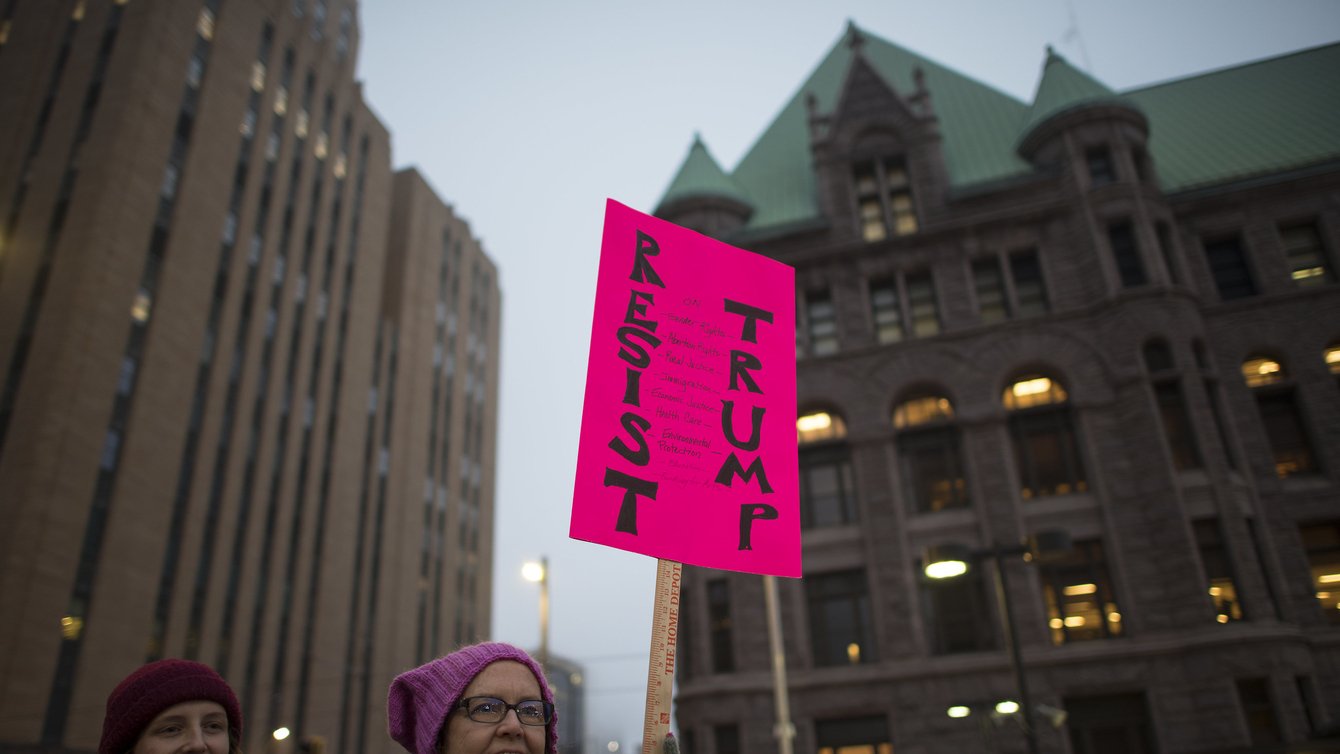Woman holds a pink sign that reads "resist trump"