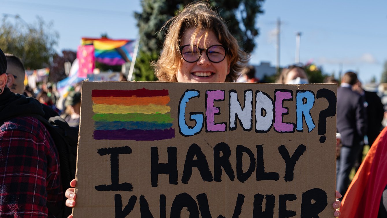 A sign at a protests saying "Gender? I hardly know her"