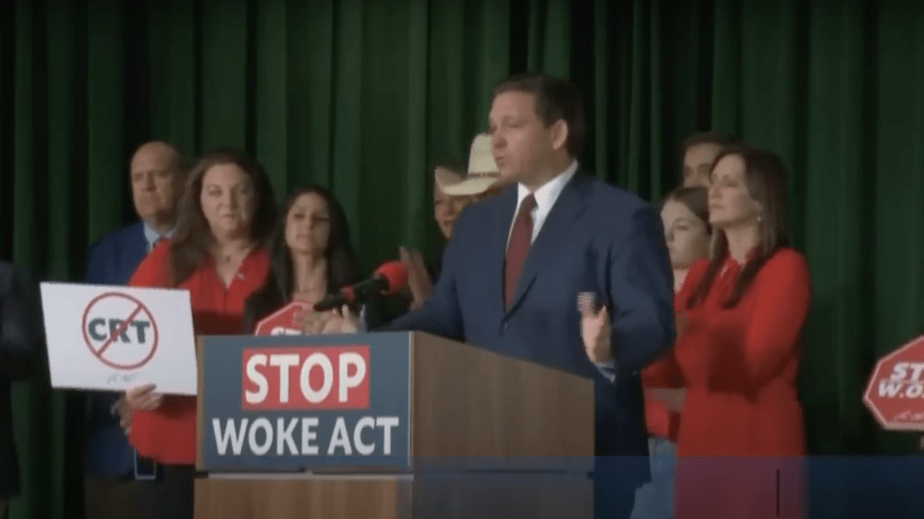 a man in a blue suit standing behind a podium with a sign that says "stop woke act"