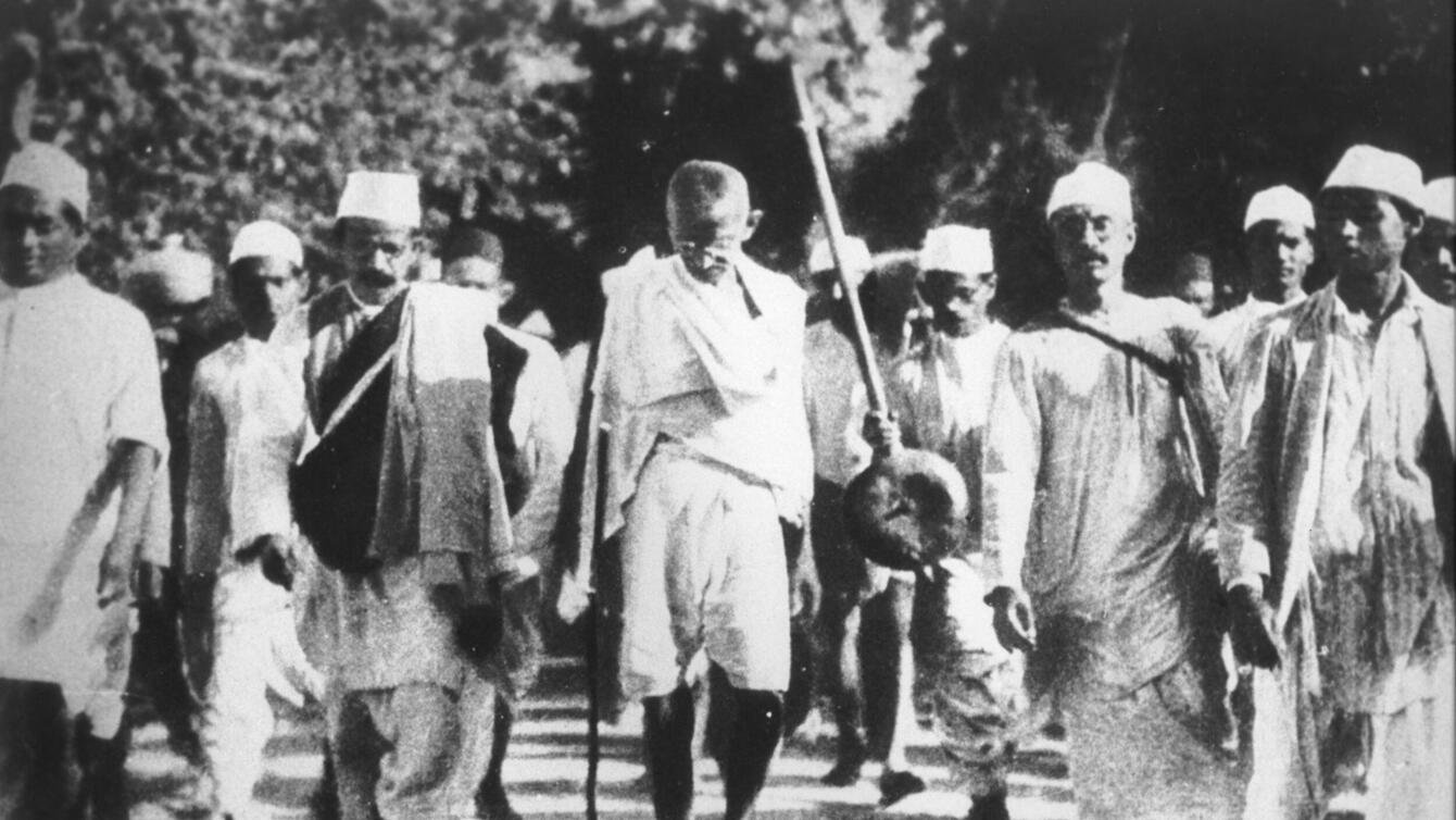 a black and white photo on people marching on the street, wearing hats and dhotis