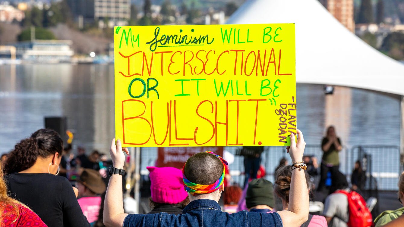A person holding a yellow sign that reads "my feminism will be intersectional or it will be bullshit."