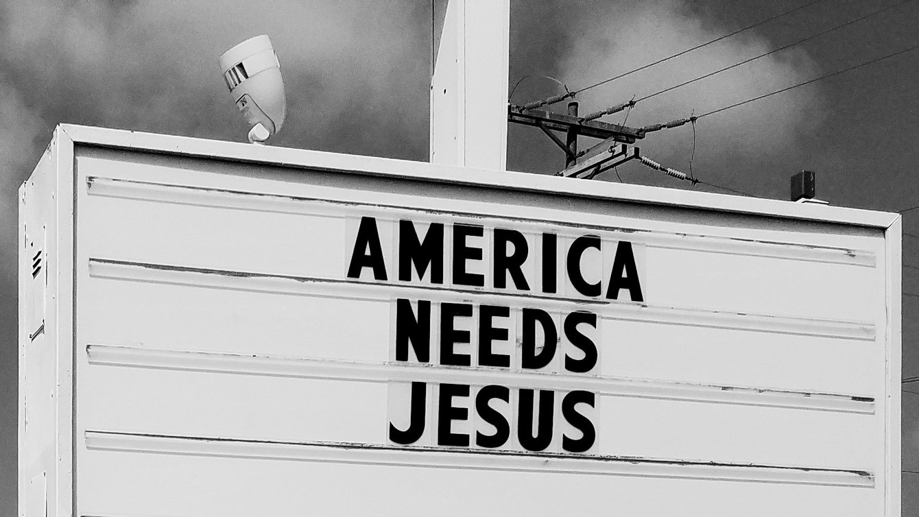 a black and white photo of a marquee sign reads "America needs jesus"