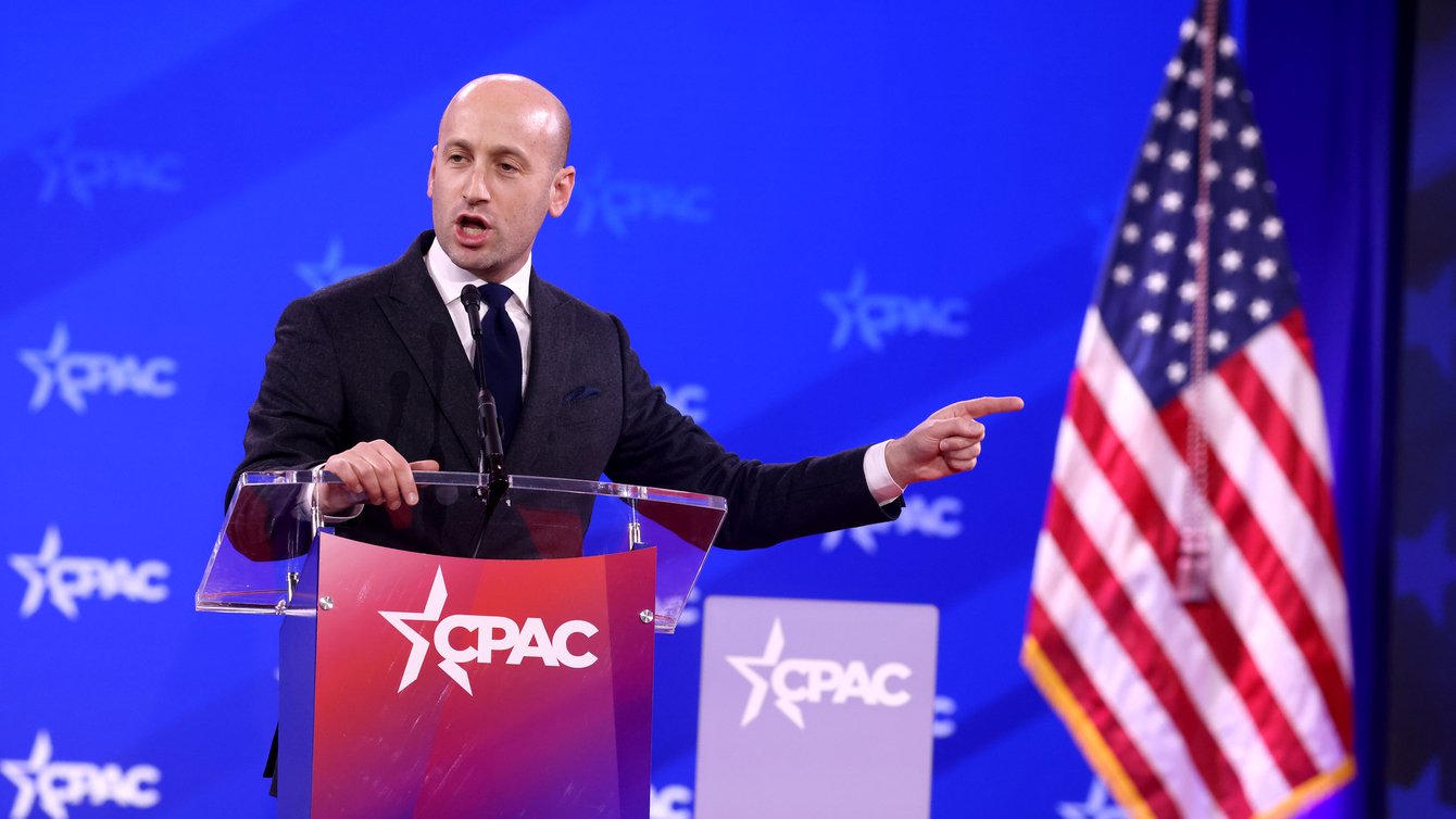 A man in a suit standing behind a podium with an American flag in the corner
