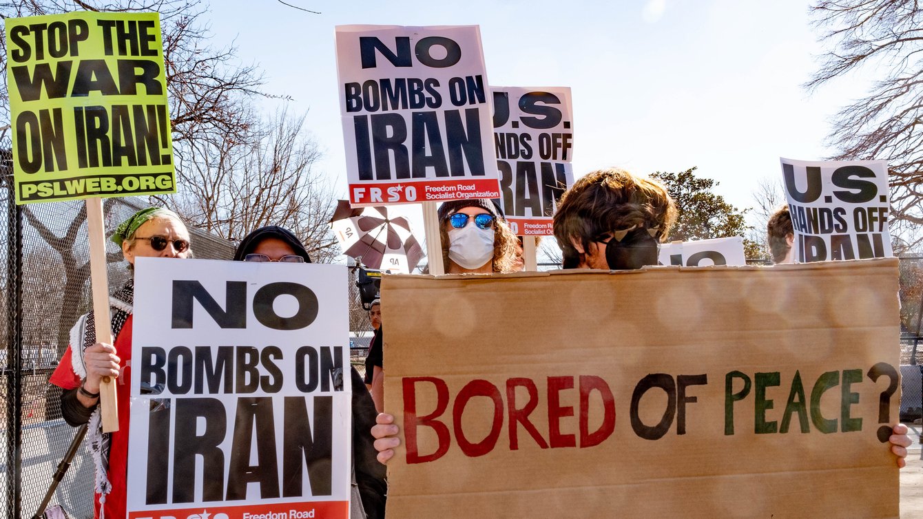 Antiwar protest signs that read "No bombs on Iran" and "Bored of Peace?"