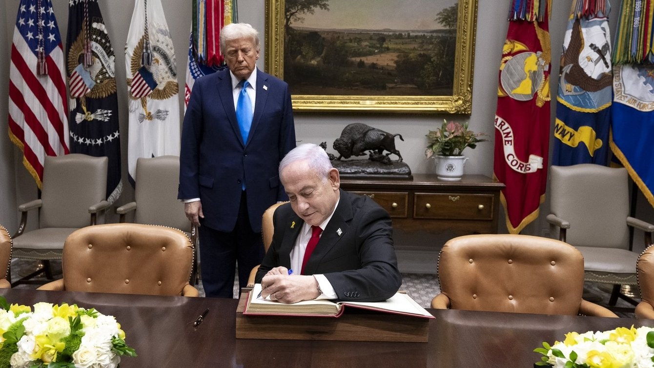 donald trump in blue suit stands behind seated benjamin netanyahu signing a document
