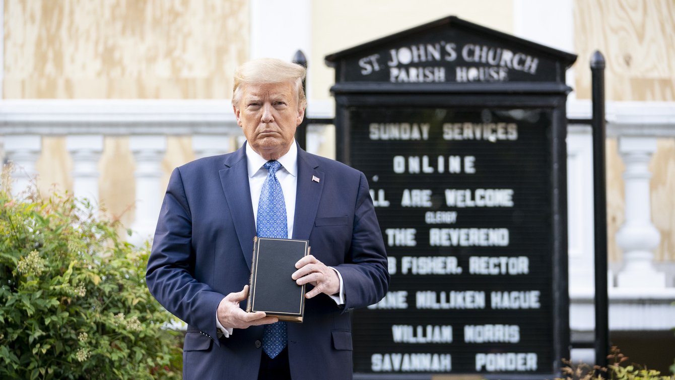 donald trump stands in front of a black sign for a church holding a bible in front of him