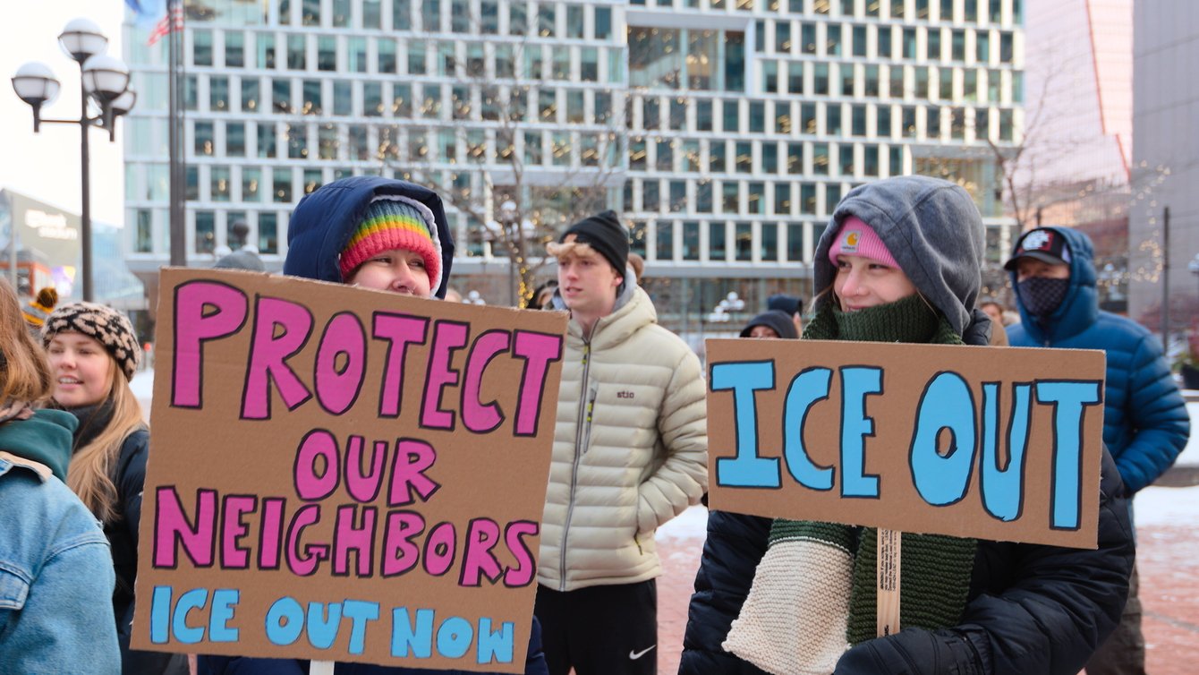 Two protestors holding sings that read "Protect our neighbors. ICE out now" and "ICE out"