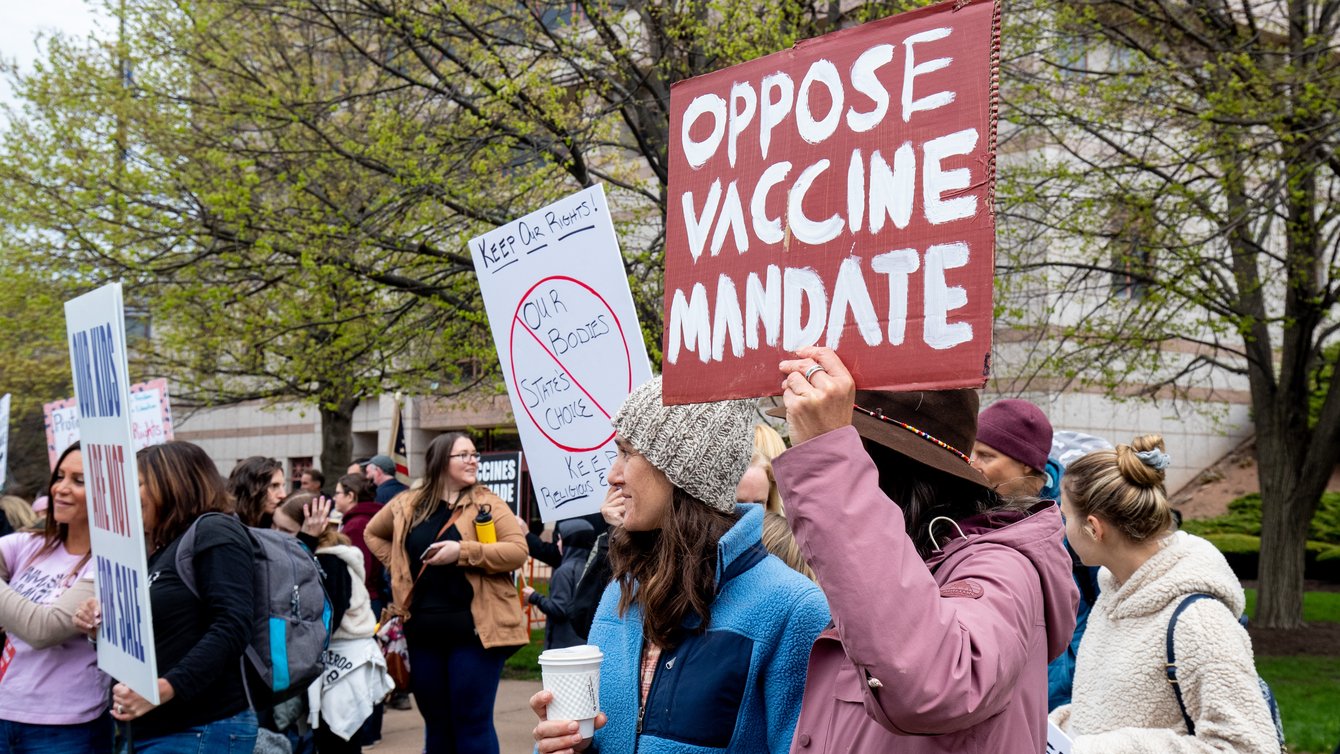 a protestor holding a sign that says "Oppose Vaccine Mandate"