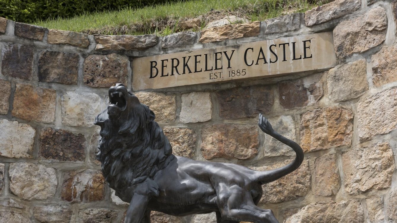 a statue of a roaring lion in front of a stone sign reading "berkeley castle"