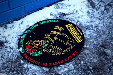 Sign left behind from an anti-abortion rally depicts dia de los muertes styled skeleton for abortion "survivors" network
