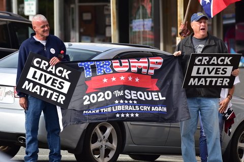 Two men holding a flag that says Trump 2020 The Sequel and banners saying "crack lives matter"