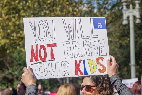 Hands holding up sign reading "You will not erase our kids"