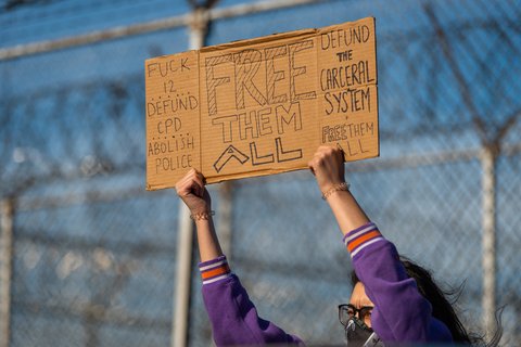 A sign on cardboard says "Fuck 12, Defund CPD, Abolish ICE, Free them All, Defund the Carceral System, Free them all"