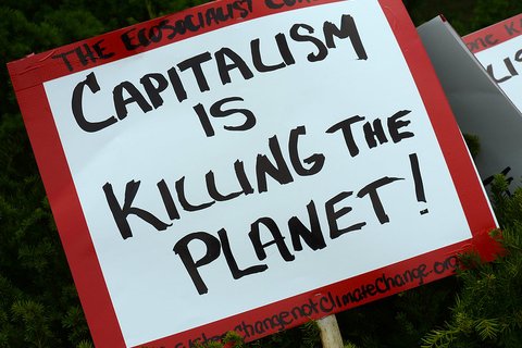 A red and white sign that says "capitalism is killing the planet!"