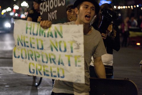 A person carrying a sign that reads "Human need not corporate greed"